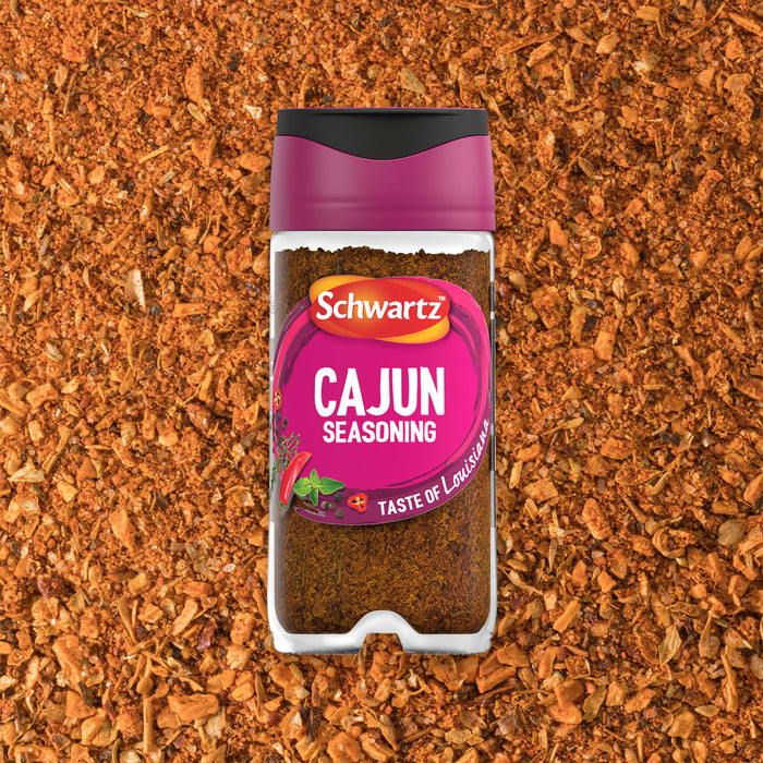A bottle of Schwartz Cajun Seasoning 44G is displayed against a background of the loose spice blend showing its coarse texture and vibrant orange color.