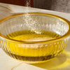 A close-up shot shows Schwartz Garlic Salt, 73G being sprinkled into a glass bowl of olive oil to create a flavorful dressing.