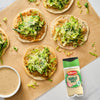 Several small chicken Caesar flatbreads are arranged on parchment paper next to a bowl of dressing and a container of Schwartz Garlic Salt, 73G.