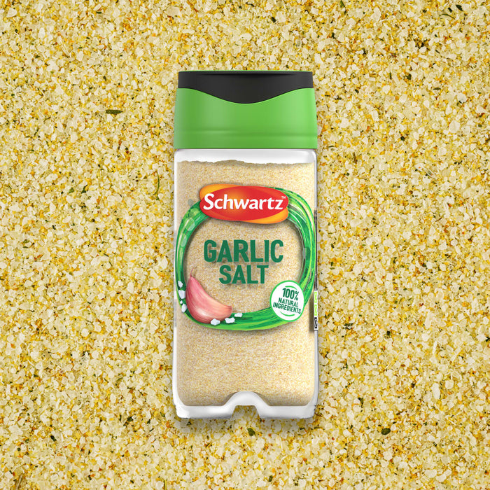 A clear jar of Schwartz Garlic Salt, 73G, is centered on a background of the coarse garlic salt seasoning.