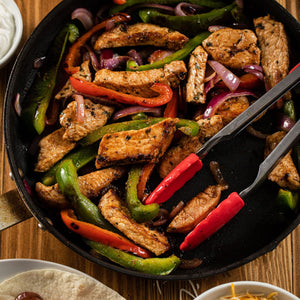 A sizzling skillet of chicken and vegetable fajitas, seasoned to perfection with Schwartz Garlic Salt, 73G, is shown with tongs ready to serve.