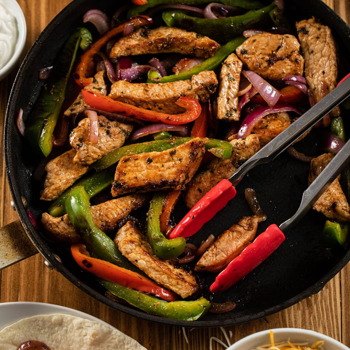 A sizzling skillet of chicken and vegetable fajitas, seasoned to perfection with Schwartz Garlic Salt, 73G, is shown with tongs ready to serve.