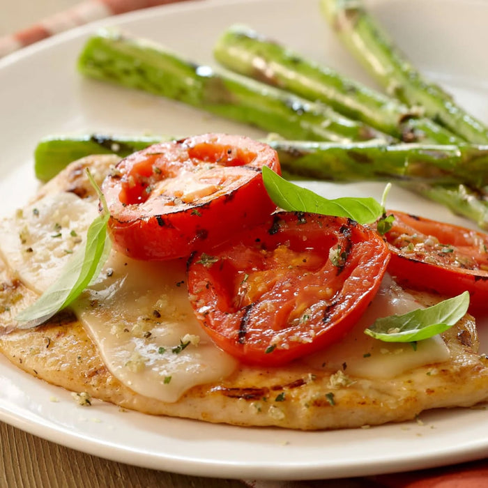 A delicious meal of grilled chicken topped with melted cheese, tomatoes, and basil, served with asparagus, shows a serving suggestion for Schwartz Garlic Salt, 73G.
