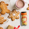 A festive holiday scene featuring decorated gingerbread cookies and a mug of hot cocoa alongside a Schwartz Ground Ginger 26G Jar used for baking.