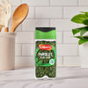 A clear jar of Schwartz Parsley, 3G sits on a white marble kitchen counter, ready to be used in a recipe.