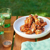 A white bowl filled with a stack of glazed chicken wings prepared with Schwartz Classic Bbq Seasoning 44G and garnished with sesame seeds and sliced spring onions on an outdoor wooden table.
