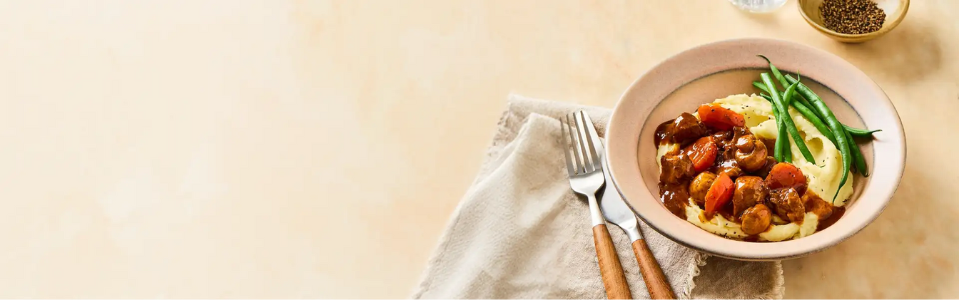 Bowl of goulash with vegetables on a beige background
