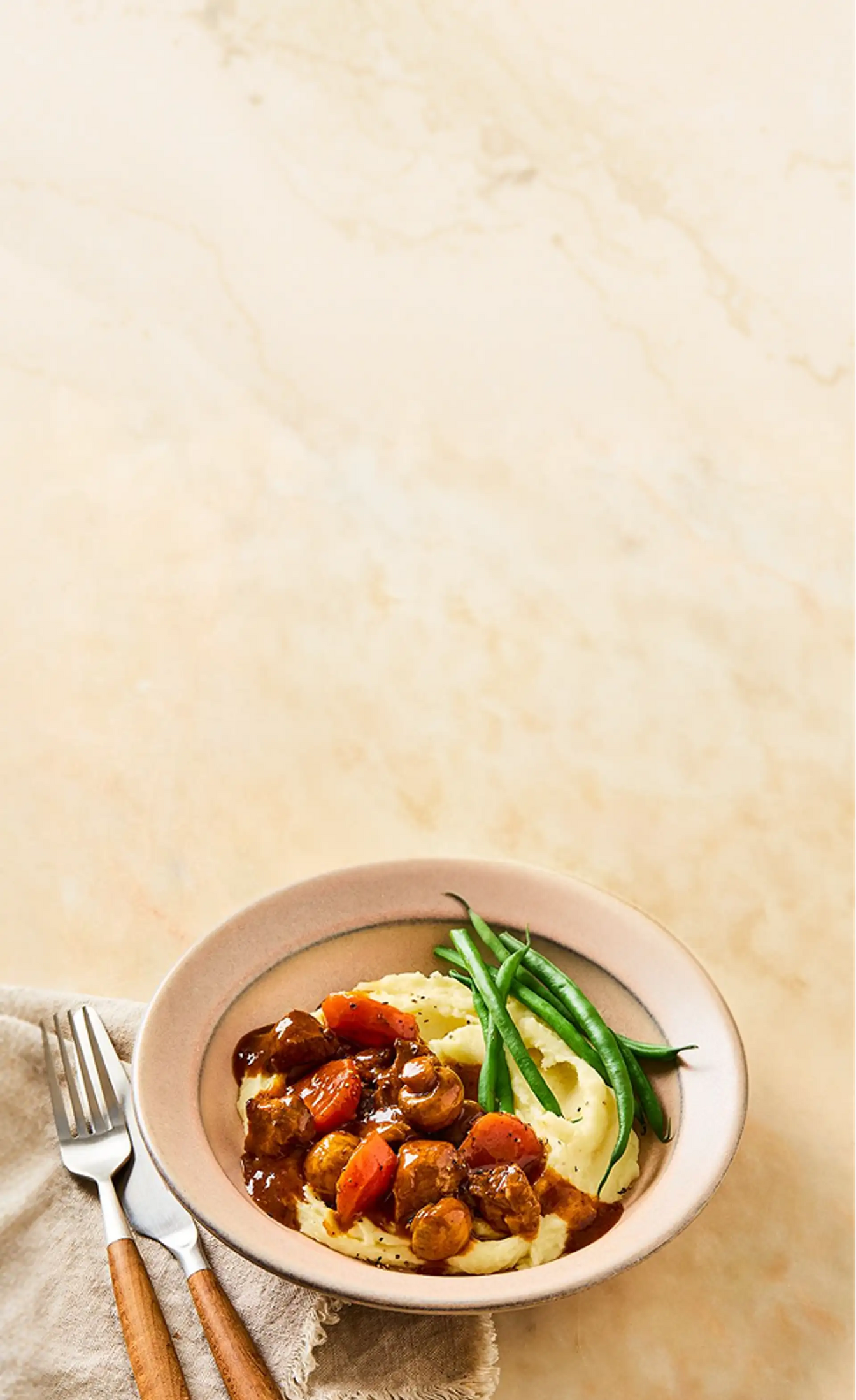 Bowl of goulash with vegetables on a beige background