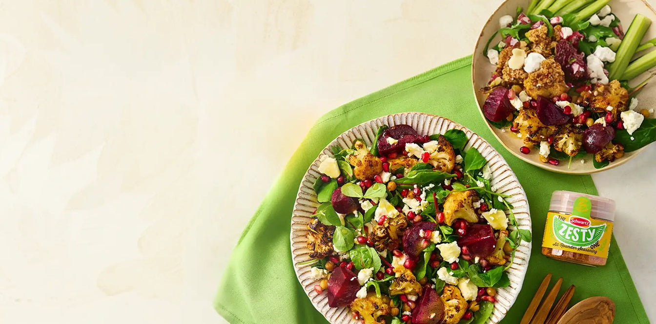 Two plates of salad with roasted vegetables on a green tablecloth, featuring Schwartz Zesty seasoning.