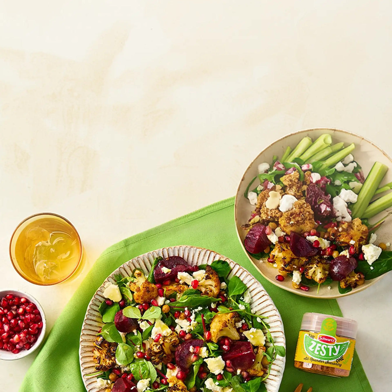 Two plates of salad with roasted vegetables on a green tablecloth, featuring Schwartz Zesty seasoning.
