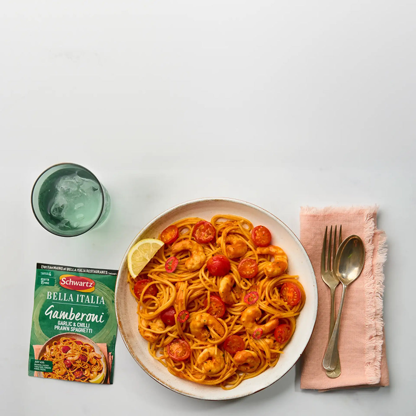 Plate of spaghetti with cherry tomatoes and a package of Schwartz Bella Italia Gamberoni on a white surface.