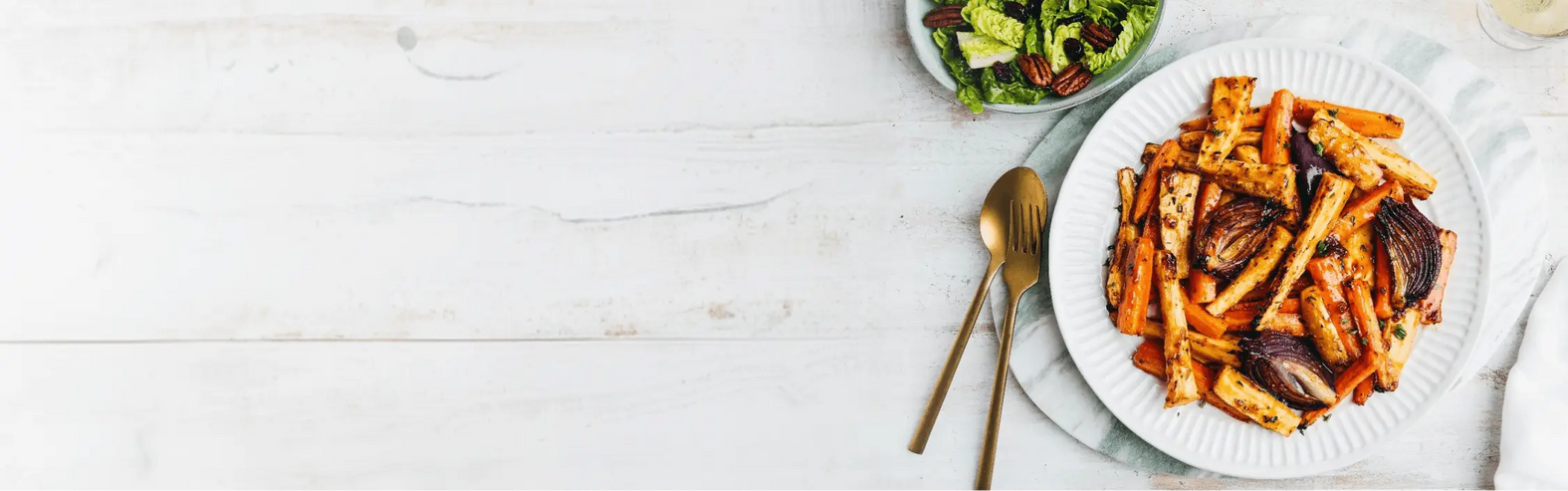 Plate of roasted vegetables with a side salad on a white table.