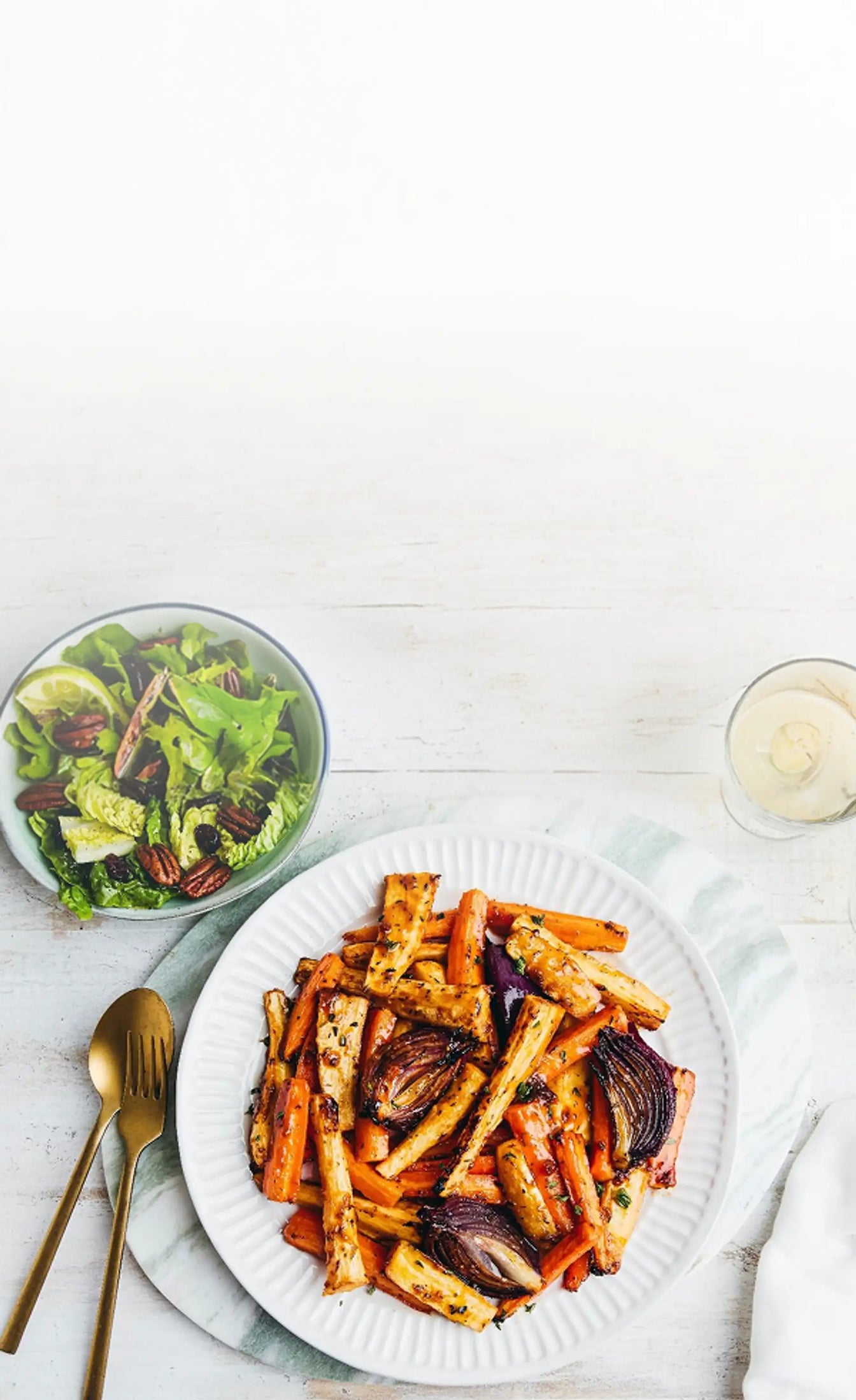 Plate of roasted vegetables with a side salad on a white table.