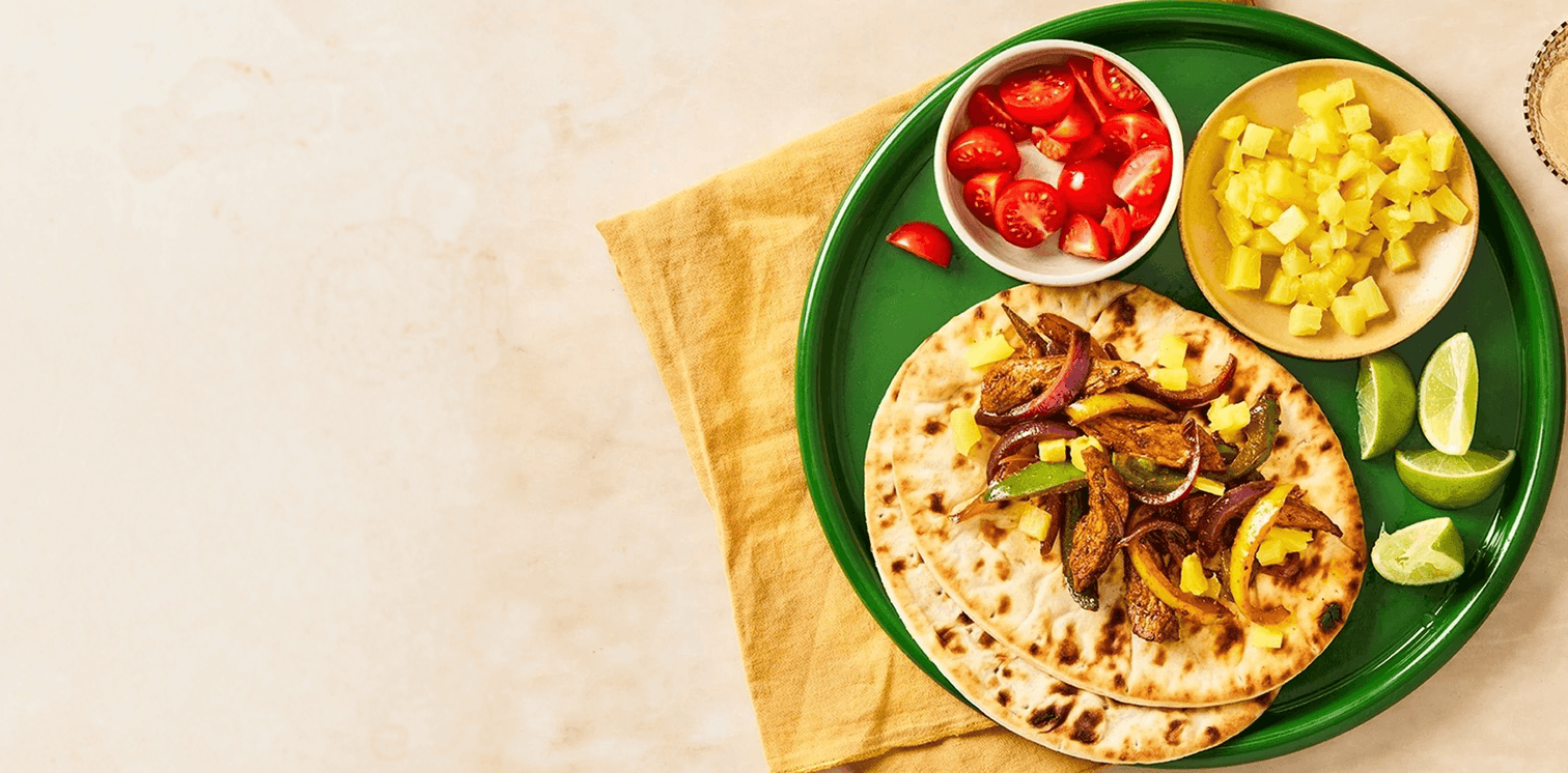 Green plate with flatbread, vegetables, and a bowl of salsa on a beige background