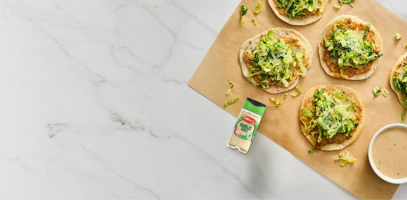 Bread slices topped with green spread on a marble surface with Schwartz garlic salt.