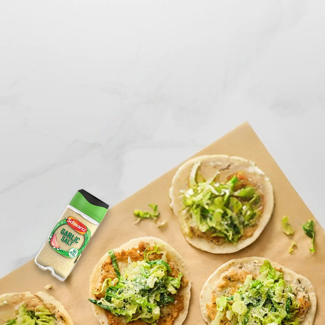 Bread slices topped with green spread on a marble surface with Schwartz garlic salt.