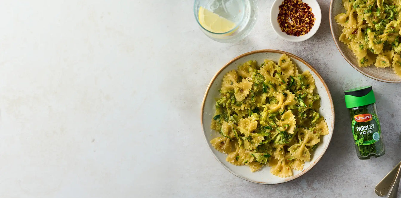 Pasta dish with a bottle of parsley flat leaf on a gray surface