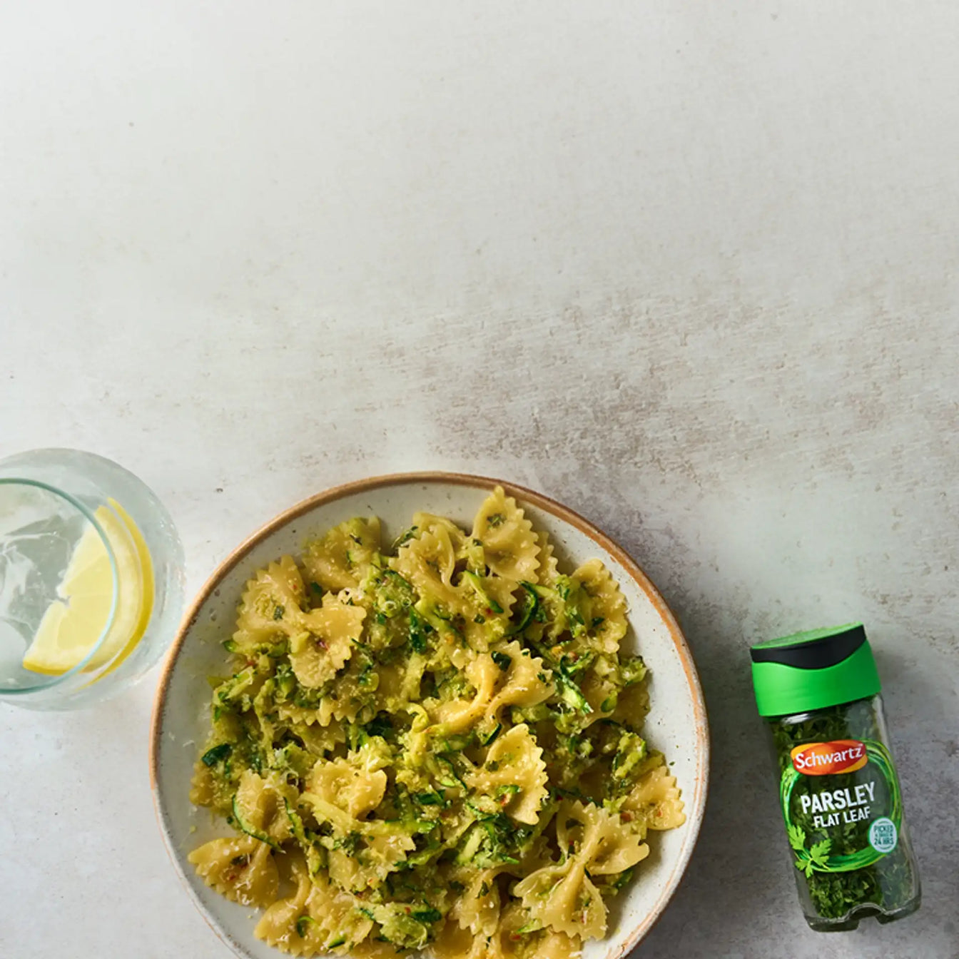 Pasta dish with a bottle of parsley flat leaf on a gray surface