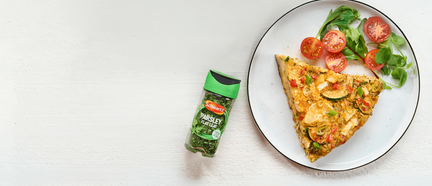 Slice of pizza with tomatoes and basil on a plate, next to a bottle of parsley flakes.