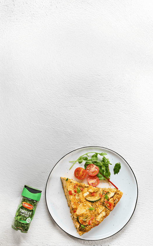 Slice of pizza with tomatoes and basil on a plate, next to a bottle of parsley flakes.