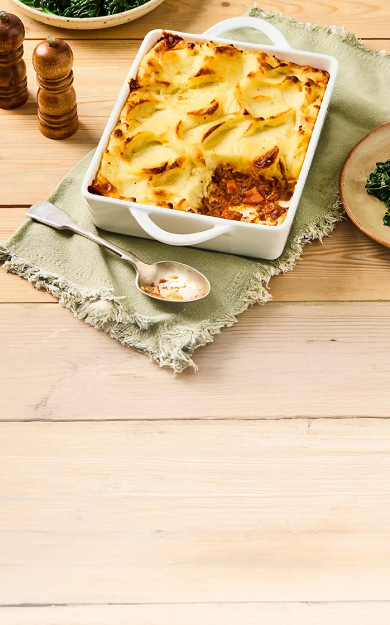 Baked dish in a white casserole dish on a wooden table with a green cloth.