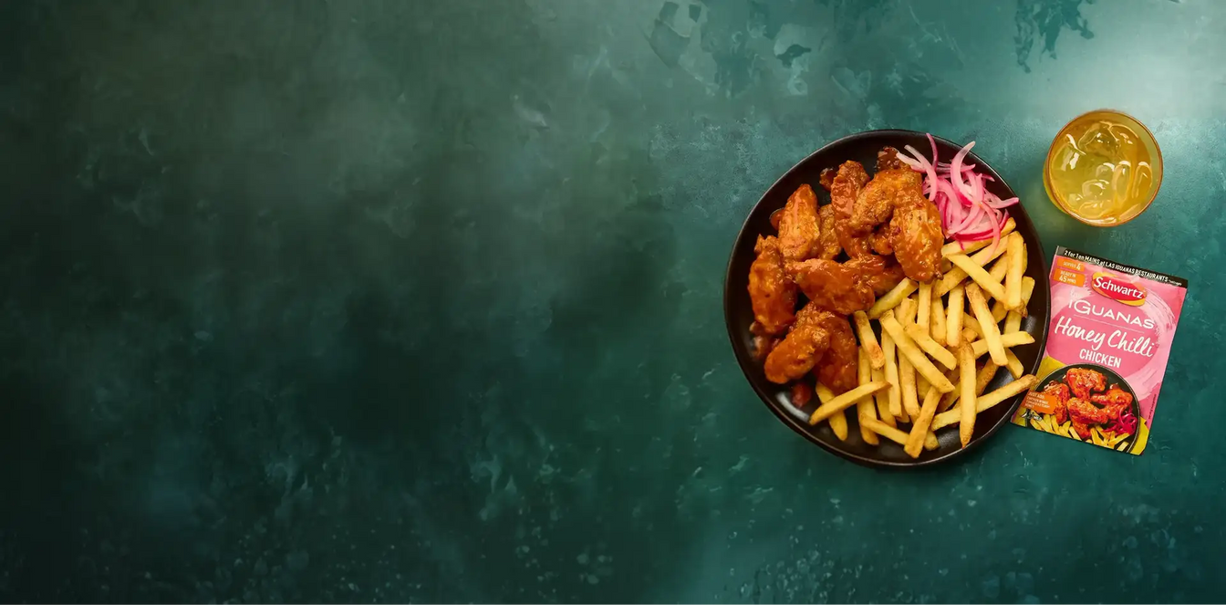 Plate of fried chicken and fries with Schwartz iguanas honey chilli chicken sauce on a dark green background