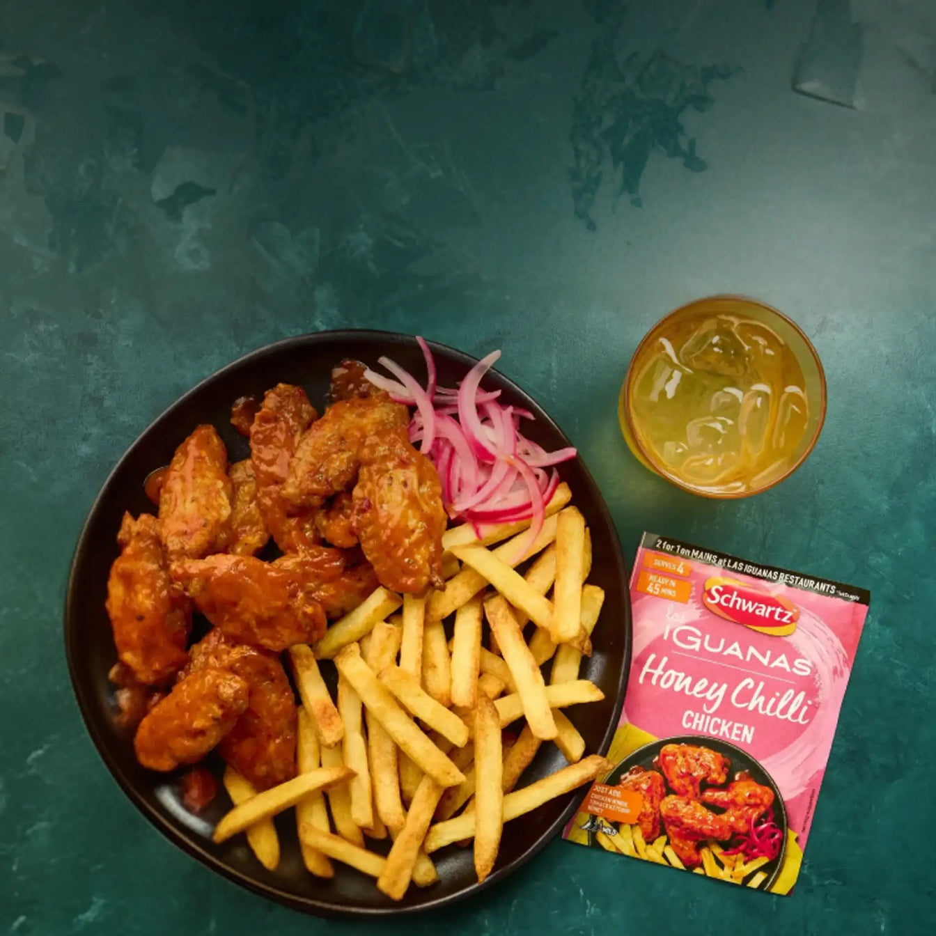 Plate of fried chicken and fries with Schwartz iguanas honey chilli chicken sauce on a dark green background