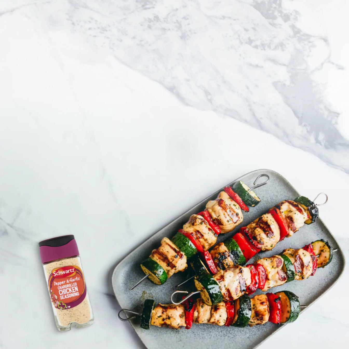 Grilled vegetable skewers on a plate with a side salad and seasoning packet on a marble surface.