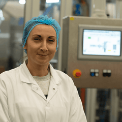 Person wearing a lab coat and hairnet in a factory setting