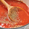 Dried Mccormick Gourmet Basil Organic herbs are sprinkled over a wooden spoon resting in a pot of red tomato sauce