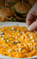 Buffalo chicken dip with blue cheese croutons on a plate, with a hand dipping a crouton into the dip.