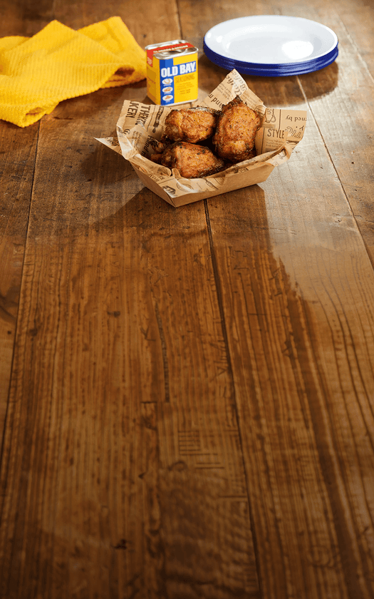 Breaded snacks in a paper basket on a wooden table with Old Bay seasoning container.