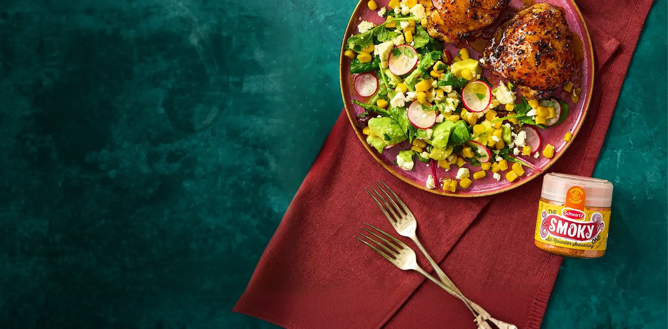 Plated dish of grilled chicken with a salad on a red napkin, featuring a jar of Smokey All Rounder Seasoning.