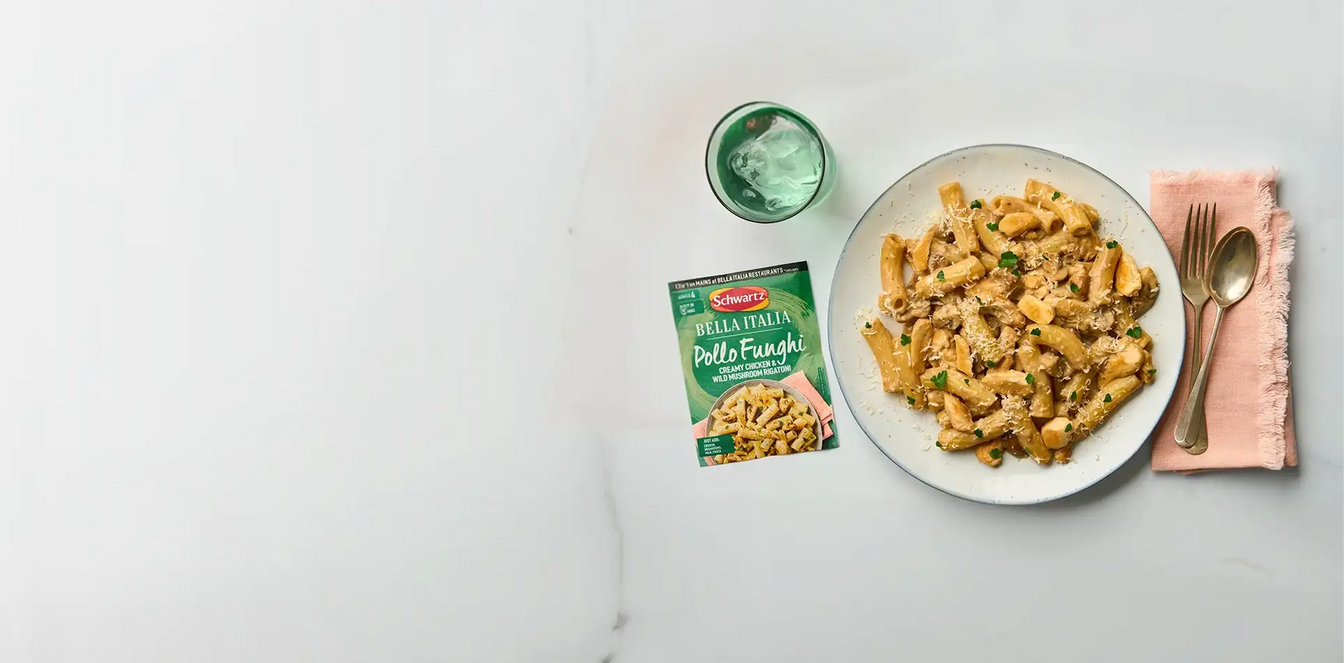 Pasta dish on a white plate with a packet of Bella Italia recipe mix on a gray background