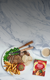 Steak with fries, peas, and a packet of creamy pepper sauce on a marble surface.