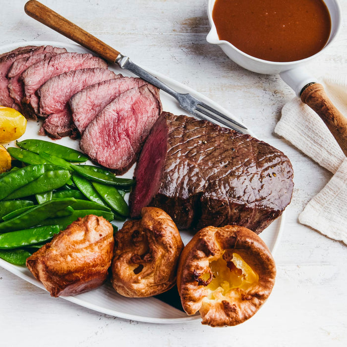 A platter of sliced roast beef is served with Yorkshire puddings, snow peas, and a side of gravy.