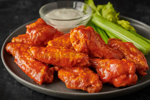 Platter of buffalo wings with celery and ranch dressing on a dark surface