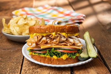 Large sandwich with turkey, lettuce, and tomato on a wooden table with chips and pickles.