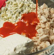 Bowl with ingredients including red sauce being poured over a mixture of chicken, cheese, and other components.