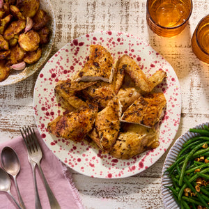 A plate of roasted chicken with potatoes and green beans on the side.