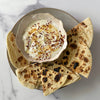 A creamy dip drizzled with honey and red pepper flakes is served in a rustic Barrel bowl, surrounded by toasted flatbread wedges for dipping.
