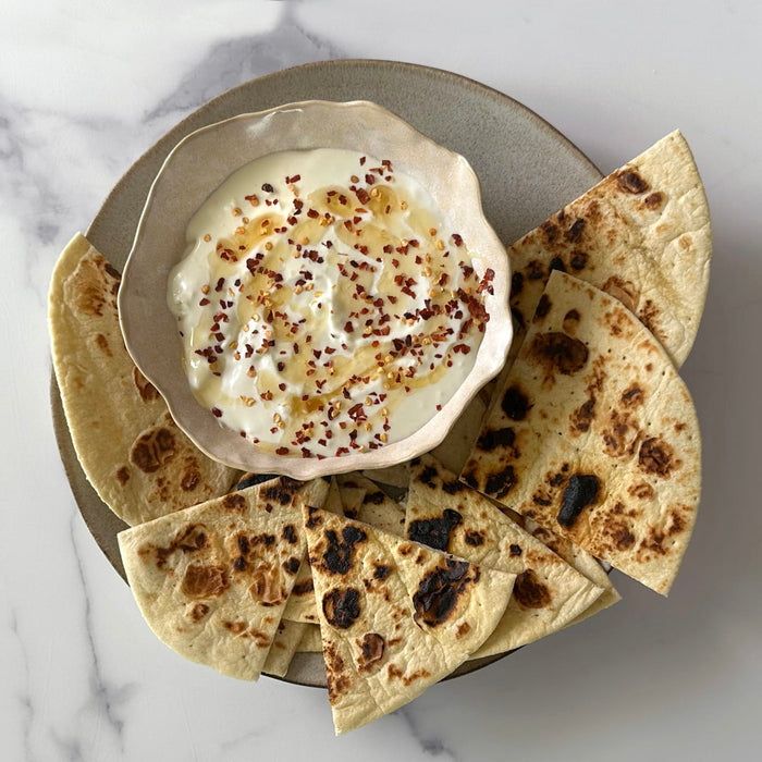 A creamy dip drizzled with honey and red pepper flakes is served in a rustic Barrel bowl, surrounded by toasted flatbread wedges for dipping.